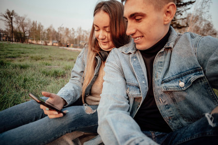 A young fashionable couple smiles while looking at the phone in the park