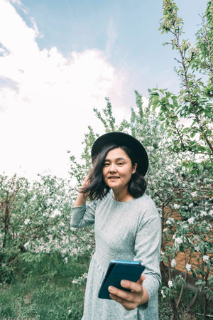 beautiful Asian girl in a hat takes a selfie on a smartphone in a blooming garden