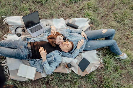Pleased caucasian relaxed students lying near opened laptop, tries to have break after work in park. Work-Life-Balance concept.の写真素材