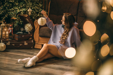 Young woman with headphones listens to music from a vinyl record, sitting on floor near a glowing Christmas tree on Christmas Dayの写真素材