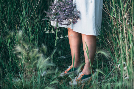 serene girls legs in sneakers amidst natures field, bouquet of flowersの写真素材