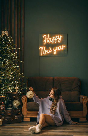 Young woman with headphones listens to music from a vinyl record, sitting on floor near a glowing Christmas tree on Christmas Dayの写真素材