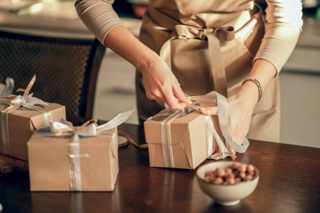 Close up womans hands tie ribbon on box for customer order. Bakery chef baking pastry and cake in...