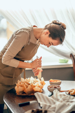 young woman applies cream to cupcakes in craft paper. the concept of food delivery. a birthday package. small business. bakery chef bakes cakes in kitchenの写真素材