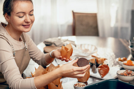 A young woman packs cupcakes in a craft. concept of food delivery. A birthday package. small business. bakery chef bakes pastries and cakes in kitchen, copy spaceの写真素材