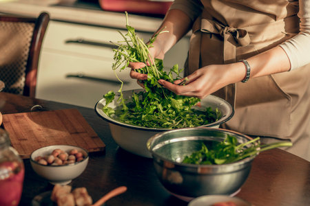 A young woman hands in an apron in the kitchen is washing parsley greens for a vegan morningの写真素材