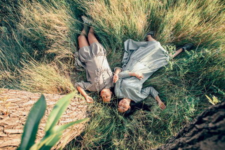 Serenity Scene : Two Asian girls in flowing dresses find tranquility on lush grass, embodying the essence of a digital detoxの写真素材