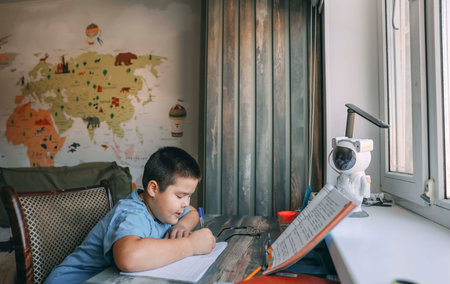 asian boy write in notebook during homework session with geography wall map, concept of home education, e-learning, tutoring servicesの写真素材
