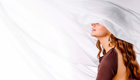 woman with long wavy red hair and golden earrings smiling under white sheer fabric in brown...