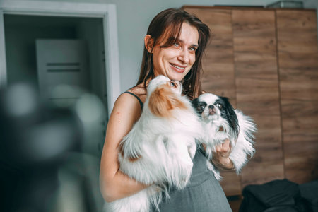 woman tenderly holding two japanese chin dogs, showcase affection and pet care at homeの写真素材