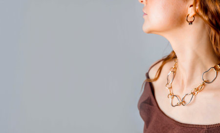 closeup of woman wearing abstract chain necklace, gold earrings, jewelry on exposed collarbones with red wavy hair, jewelry design, luxury, web bannerの写真素材