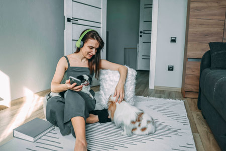 woman in casual wear with headphones interacting with her dogs in a modern living space, capturing a moment of joyful pet companionshipの写真素材