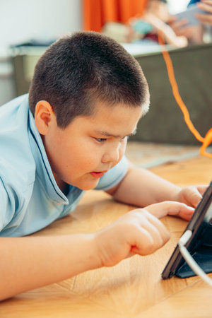 Closeup portrait of a boy who looks into the phone sitting on the floor, phone chargingの写真素材