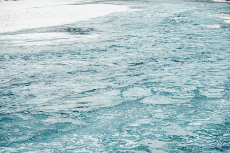 A serene river flows through a snowy landscape, surrounded by mountains. The water is clear and...