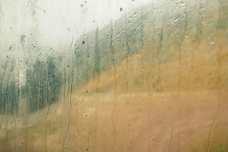 A foggy view from a cable car window, showing blurred mountains and rain droplets on the glass. The...