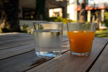 a glass of water and a glass of orange juice on an old wooden table, the healthiest drink of the...