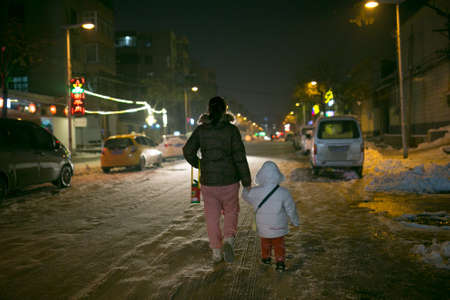 Mother and daughter walking on the snowy road during winter nightの写真素材