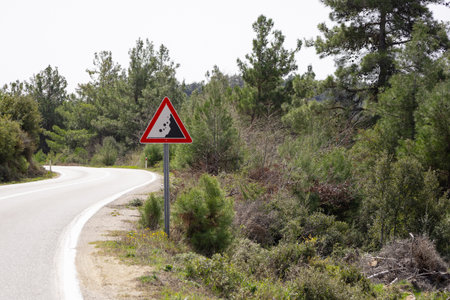 Winding Road with Landslide Warning Sign in Forested Areaの写真素材