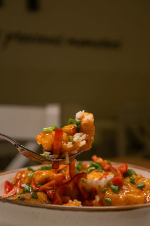 Close up of a fork lifting a piece of spicy chicken with rice and vegetables