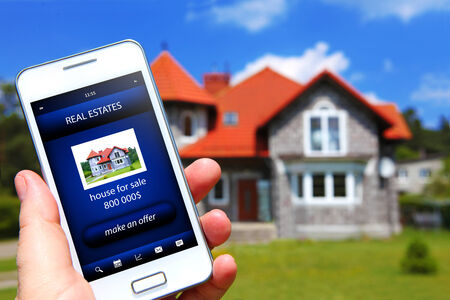 hand holding mobile phone with house sale offer and house as a backgroundの写真素材