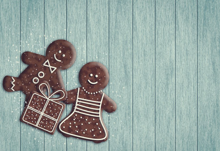 gingerbread man and gingerbread woman holding present on wooden desk with place for text