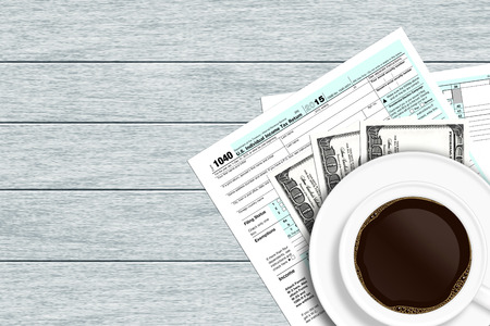 1040 tax form with dollars and coffee lying on wooden desk with place for textの写真素材