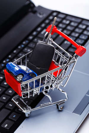 Car and key in shopping trolley above laptop keyboardの写真素材