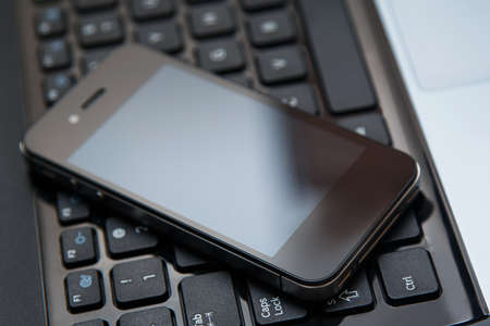 Smartphone lying above laptop keyboardの写真素材