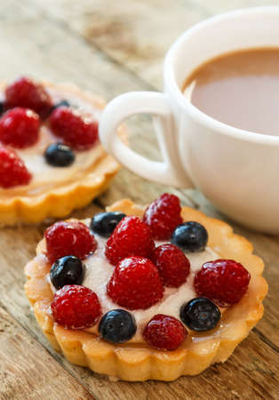 Cup of coffee and sweet cakes with berries on wooden tableの写真素材