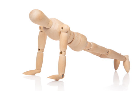 Small wooden dummy during push ups on white background