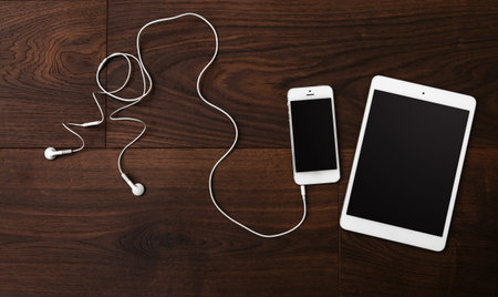 Smartphone and tablet with earphones on wooden surface