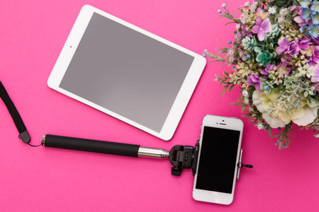 Smart phone on a selfie stick and tablet pc on pink background