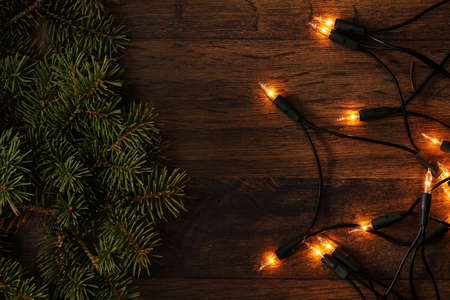 Christmas lights and branches of spruce on wooden surfaceの写真素材