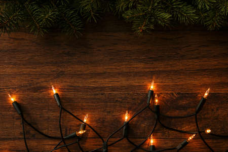 Christmas lights and branches of spruce on wooden surfaceの写真素材