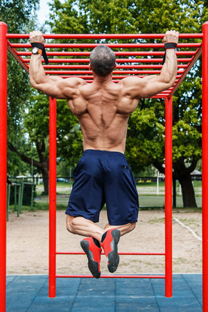 Muscular man doing pull-ups on horizontal bar