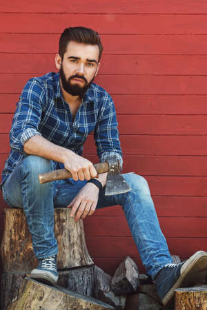 Handsome bearded man with axe sitting on stumpの写真素材