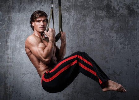 Muscular man during workout with suspension straps