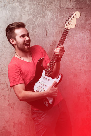 Handsome guy with electric guitar beside a dirty wall