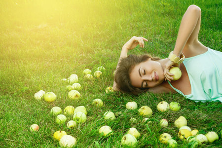 Lovely woman is lying on the grass with a lot of apples around herの写真素材