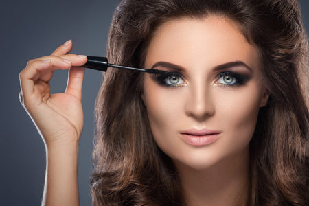 Beautiful woman with beautiful make-up applying mascara on her lashes