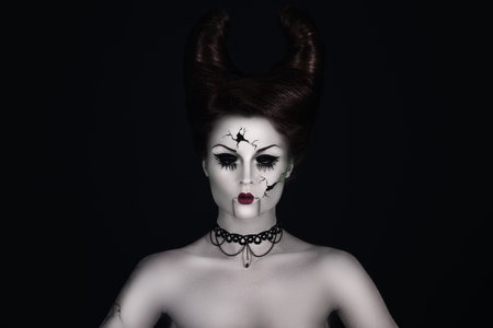 Model in creative image. Talking broken doll with horns on her head.