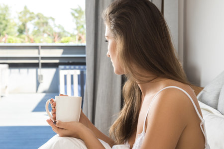 Beautiful woman drinking coffee or tea in bedroom at the morning