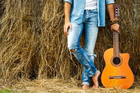 Male legs and acoustic guitar beside the haystackの写真素材