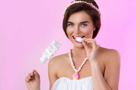 Happy beautiful woman with marshmallows on the skewer on pink backgroundの写真素材