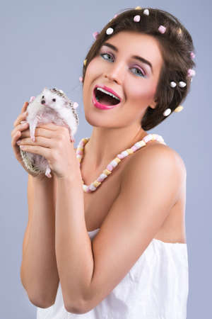 Beautiful woman with a creative hairstyle which made from marshmallow is holding a cute little hedgehogの写真素材