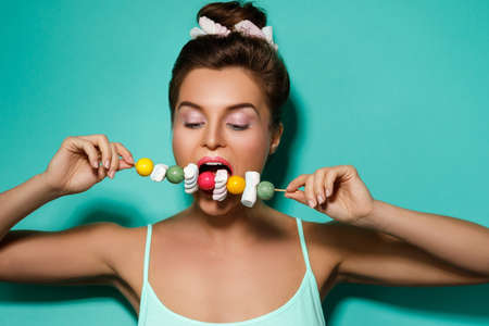 Happy woman with colorful makeup and sweet candies on skewer against cyan backgroundの写真素材