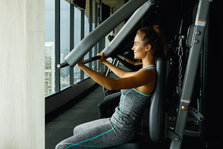 Young and sporty woman using press machine in the gym