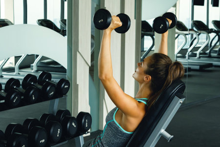 Young and beautiful woman working out with dumbbells in gym