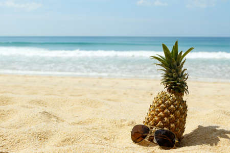 Pineapple fruit and sunglasses on the beachの写真素材