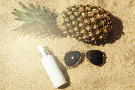 Pineapple, sunglasses and sunscreen lotion on the beachの写真素材